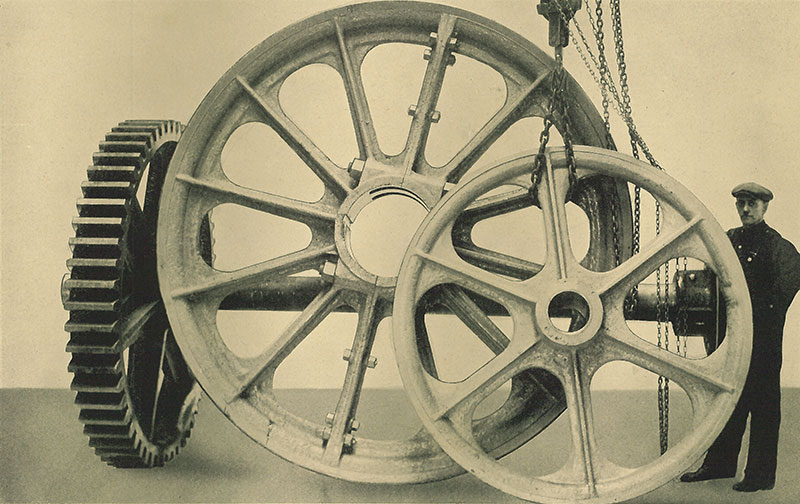 Un travailleur est debout à côté de trois immenses roues en métal.