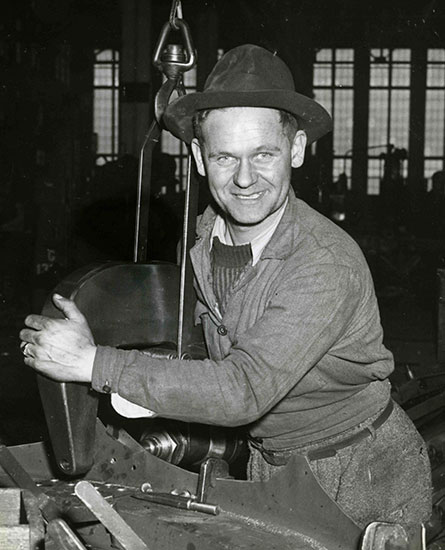 Un homme portant un chapeau et tenant une pièce en métal dans ses mains.