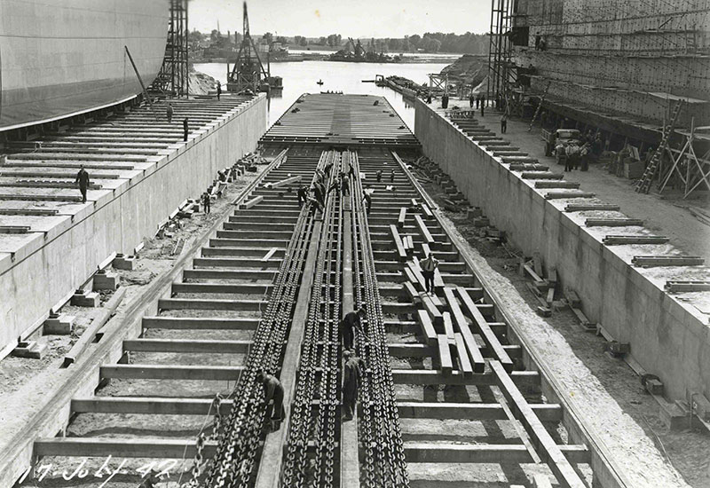 Plusieurs hommes travaillent sur la voie ferrée inclinée du chantier naval.