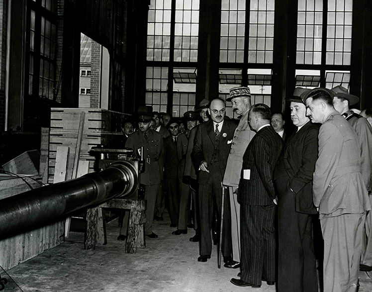 Un homme portant un képi entouré de plusieurs hommes regardant un canon.