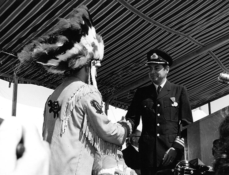 Un homme en uniforme serrant la main d'un Amérindien coiffé de plumes.